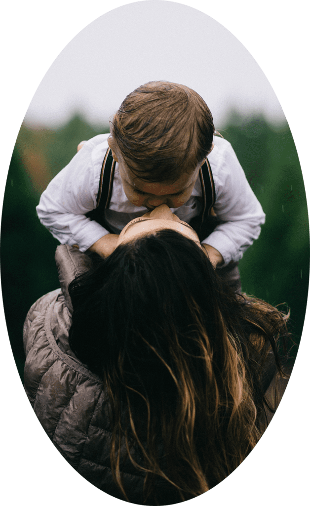 Child kissing adult in outdoor setting.