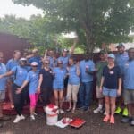Group of people in blue shirts posing outdoors under a tree.