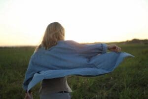 Person outdoors wrapping themselves in a blue blanket at sunset.
