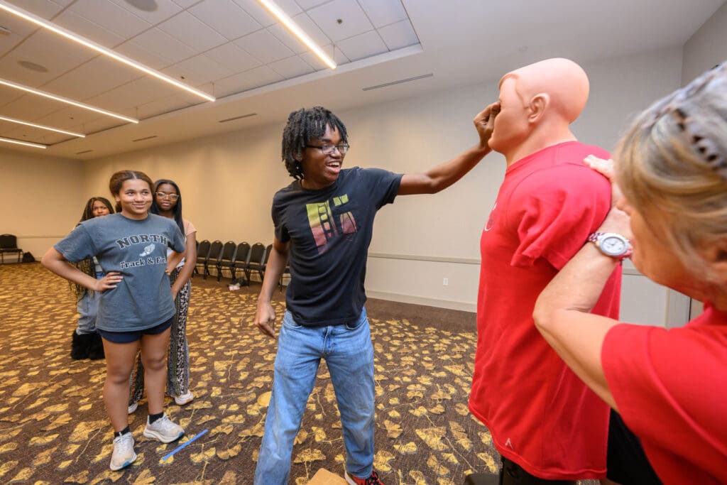 A man playfully touches another man's face in a social setting with onlookers.