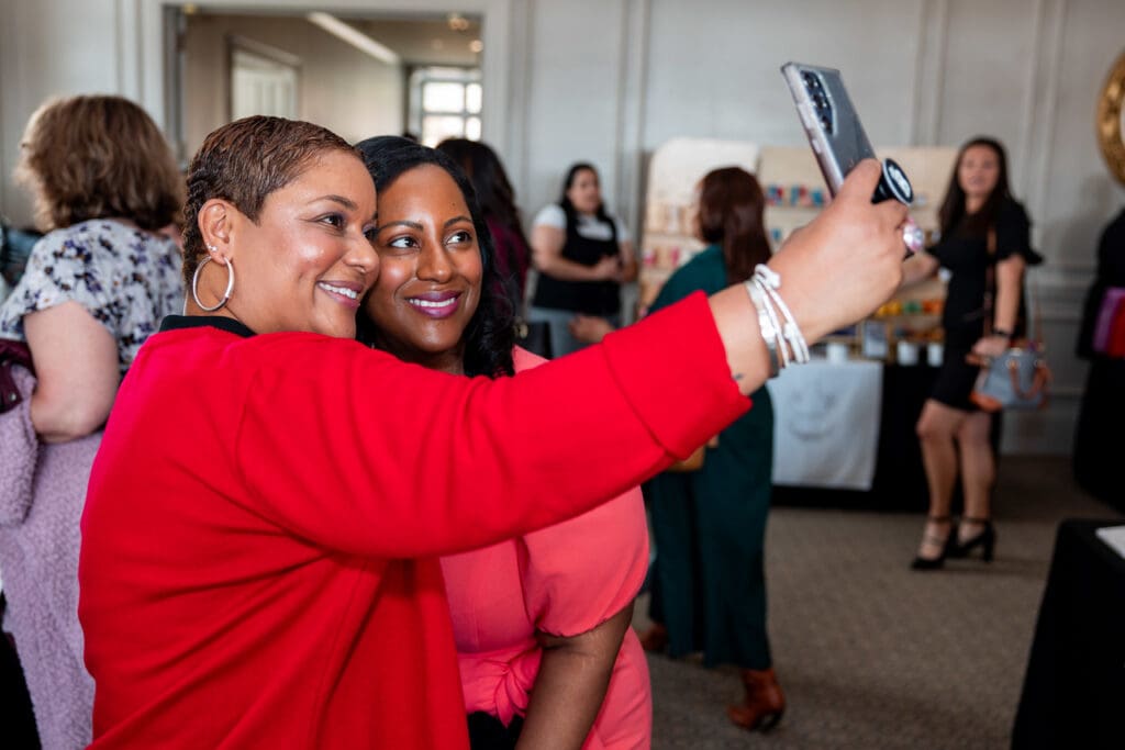 Two women smiling and taking a selfie at a social event.