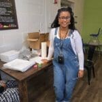 Smiling person in overalls near a table.